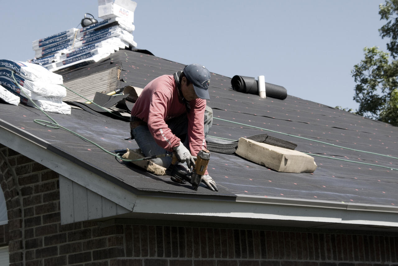 A roofer replacing shingles on a residential roof, absorbed in his work